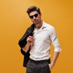 attractive-brunet-man-stylish-white-shirt-trendy-sunglasses-poses-orange-background-holds-black-jacket