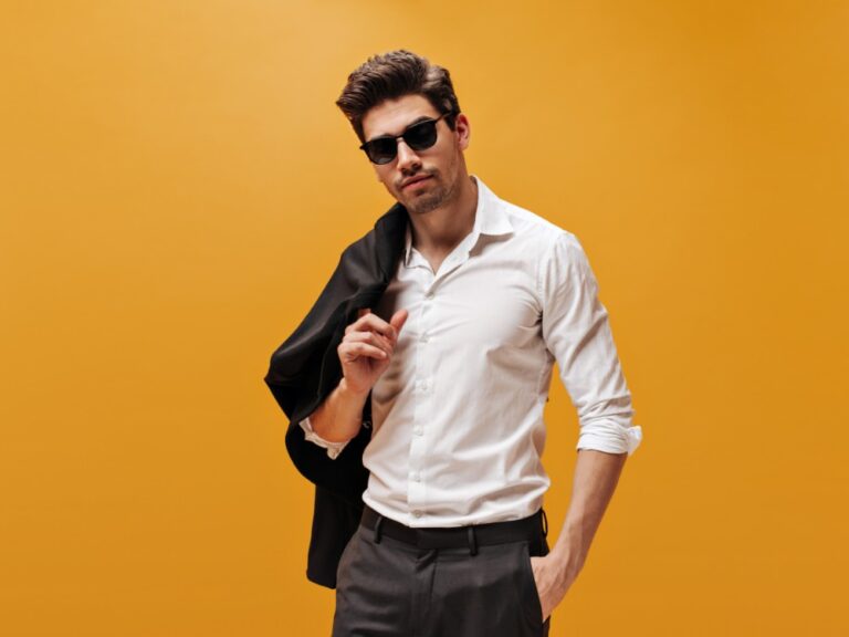 attractive-brunet-man-stylish-white-shirt-trendy-sunglasses-poses-orange-background-holds-black-jacket